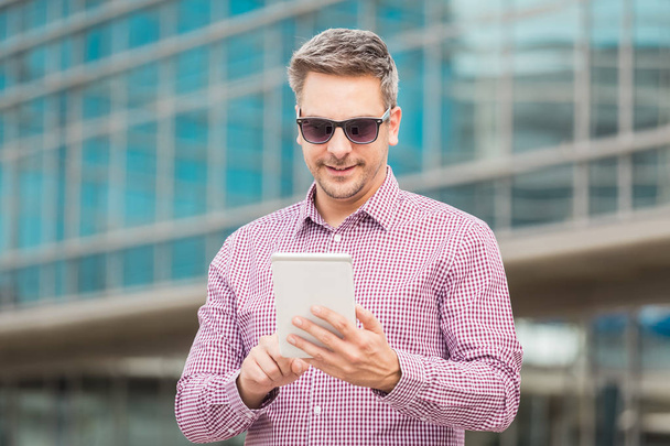Portrait d'un homme d'affaires utilisant une tablette numérique avec un immeuble de bureaux en arrière-plan
. - Photo, image