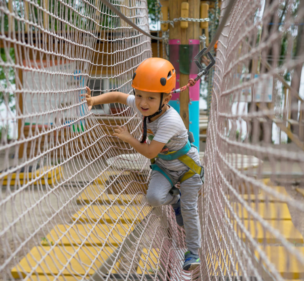 ein kleiner glücklicher und lächelnder Bergsteiger bindet einen Knoten an einem Seil. eine Person bereitet sich auf den Aufstieg vor. lernt das Kind, einen Knoten zu knüpfen. Prüfung der Versicherung für das Klettern. - Foto, Bild