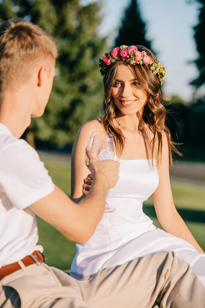 beautiful wedding couple clinking with wine glasses on picnic - Fotografie, Obrázek