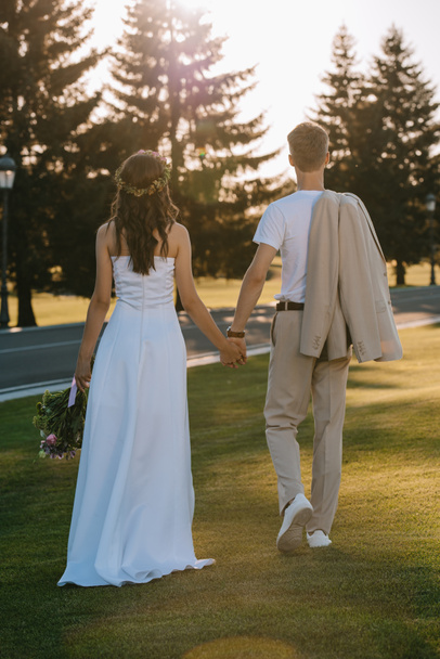 back view of wedding couple holding hands and walking outdoors - Foto, imagen
