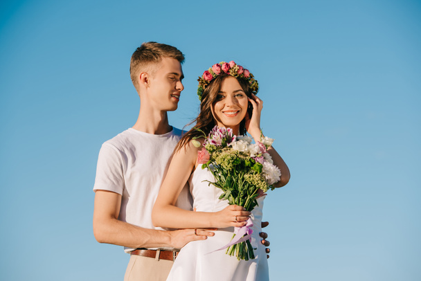 beautiful wedding couple holding bouquet and posing against blue sky - Фото, изображение
