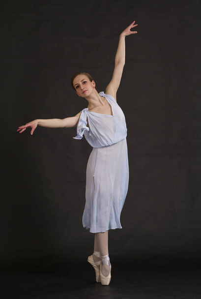 Young ballerina in blue dress isolated on black. Dance school. - Foto, afbeelding