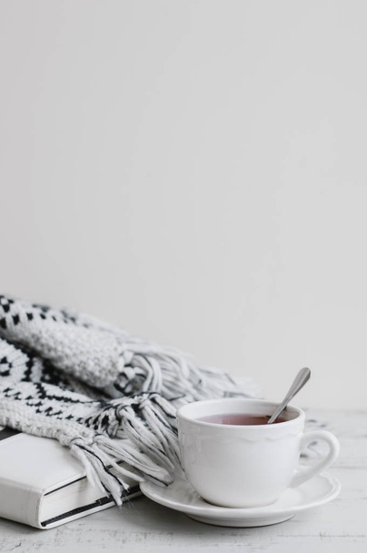 vertikaler Hintergrund mit weißer Tasse rotem Tee, Buch und Strickdecke auf Holztisch, Kopierraum. Hygge-Konzept. Teepause - Foto, Bild