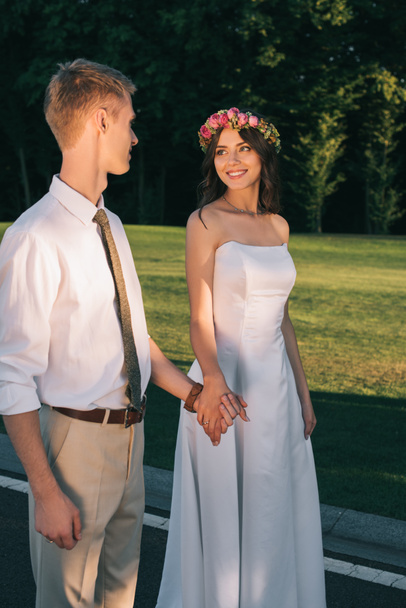 beautiful romantic young wedding couple smiling each other and walking together in park - Photo, image
