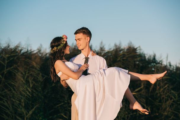 heureux jeune marié portant belle mariée dans le parc
   - Photo, image