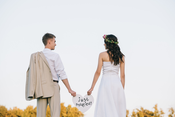 Achteraanzicht van jonge bruidspaar houden hart met net getrouwd inscriptie - Foto, afbeelding
