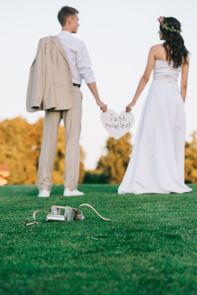 Arkadan Görünüş yeşil çimenlerin üzerinde duran ve sadece evli yazıt ile kalp tutan genç düğün çift - Fotoğraf, Görsel