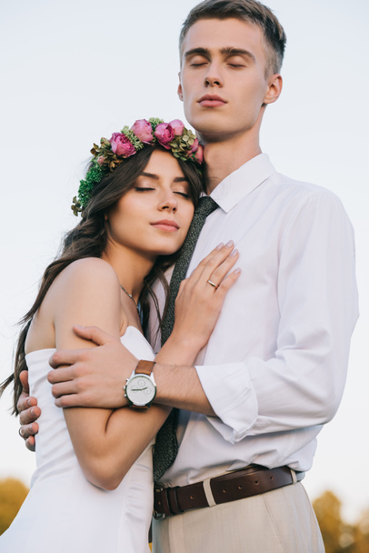 низкий угол зрения красивой романтической молодой свадебной пары обнимая и стоя с закрытыми глазами
 - Фото, изображение