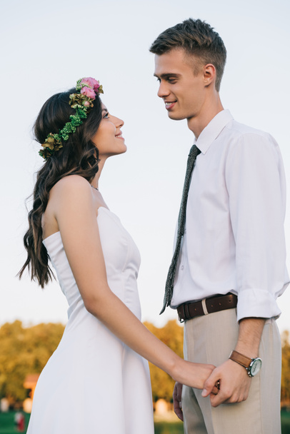 beautiful romantic young wedding couple holding hands and smiling each other  - Photo, Image