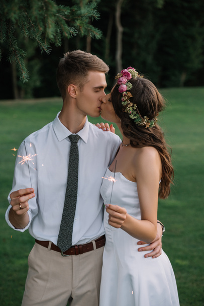 elegant romantic young wedding couple kissing and holding sparklers outdoors - Фото, изображение