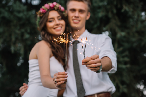 close-up view of happy young wedding couple holding sparklers and smiling at camera - Valokuva, kuva