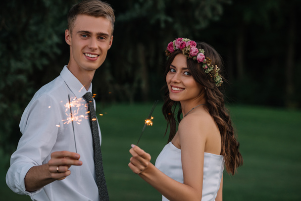 美しい幸せな若い結婚式カップル花火を押しながらカメラに笑顔 - 写真・画像
