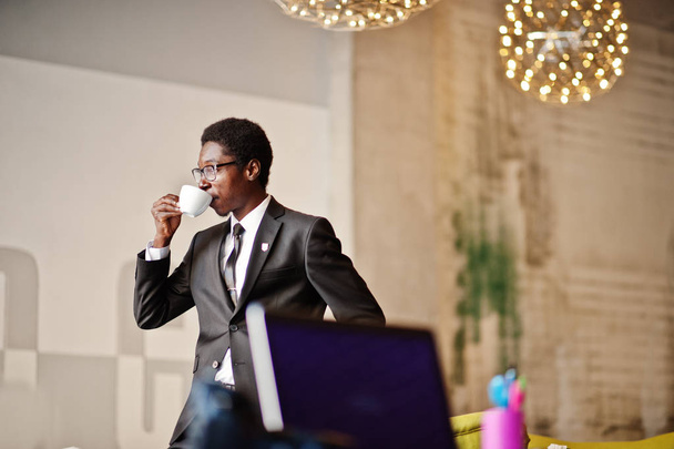 Business afrikkalainen amerikkalainen mies pukeutua musta puku ja lasit toimistossa, juo aamulla kahvia ennen työpäivää
. - Valokuva, kuva