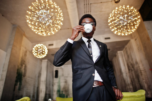 Business african american man wear on black suit and glasses at office, drinking morning coffee before work day. - Foto, Imagem