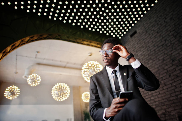 Homme d'affaires afro-américain porter sur costume noir et lunettes au bureau regardant sur téléphone portable contre les lumières futuristes
. - Photo, image