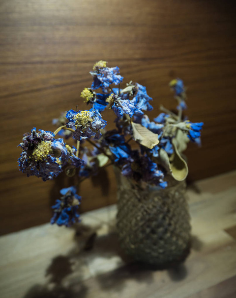 La flor seca en vidrio puesta en tablero de madera de madera, en tono de luz cálida, luz borrosa alrededor
. - Foto, imagen