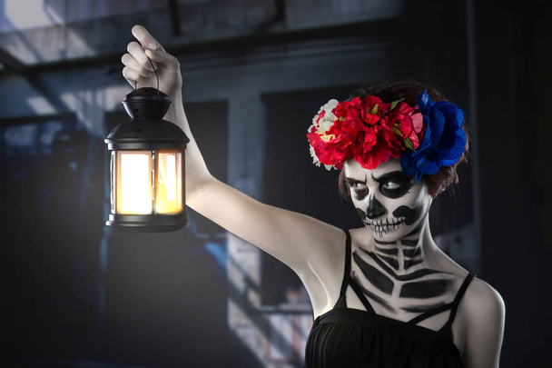Halloween witch. Beautiful woman wearing santa muerte mask casting spell near light bulb - Photo, Image