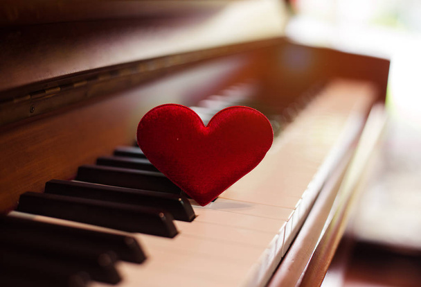 NO foco seletivo de pequeno coração vermelho colocar em teclas de piano, tom de luz quente, fundo de design de luz embaçada
. - Foto, Imagem