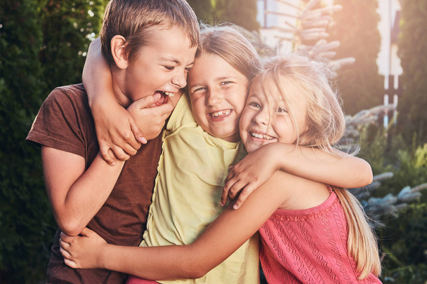 Retrato de pequeños amigos felices divirtiéndose en el patio. Tres lindos amiguitos abrazándose y jugando
. - Foto, Imagen