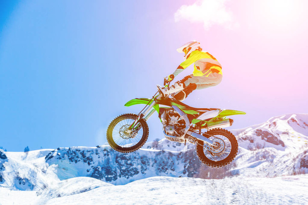piloto em uma motocicleta em voo, salta e decola em um trampolim contra as montanhas nevadas
 - Foto, Imagem