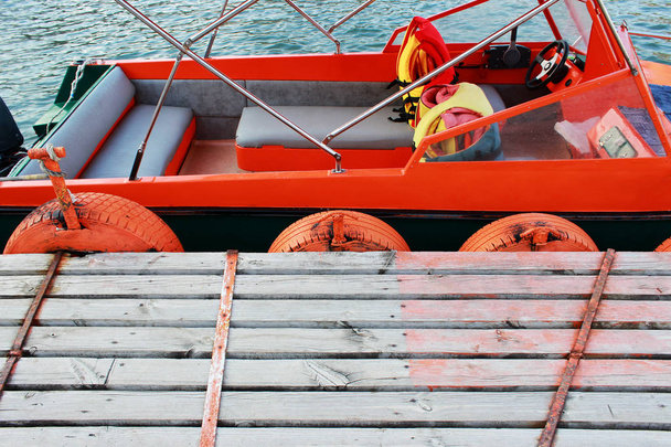małej łodzi zacumowane na drewnianym molo nad morzem. Opony od felgi ochrony statku przed uszkodzeniem i są pomalowane farbą pomarańczowy dla lepszej widoczności. - Zdjęcie, obraz