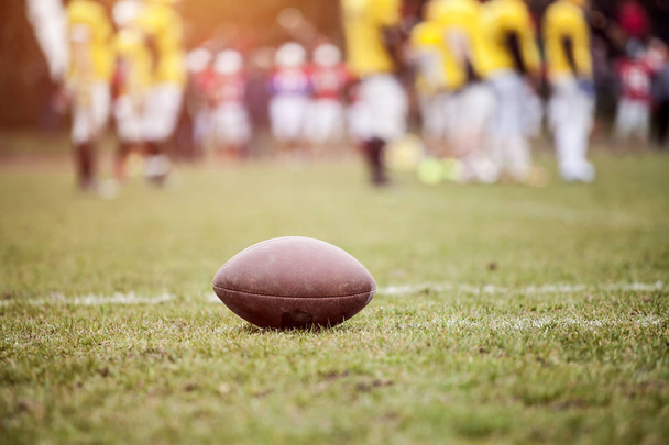 Close up of an american football on the field, players in the background - Фото, изображение