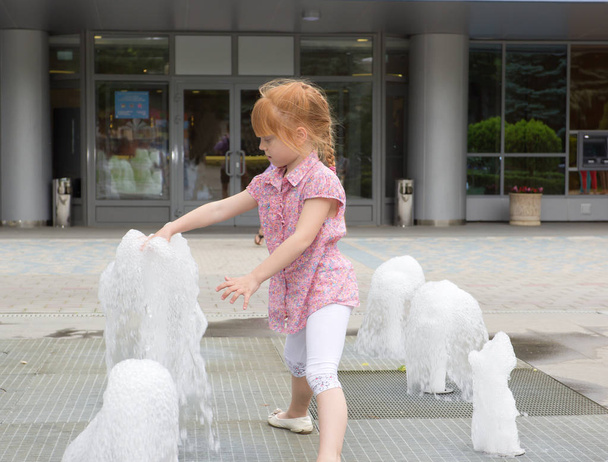 Cheerful red-haired little girl at the fountain - Фото, изображение