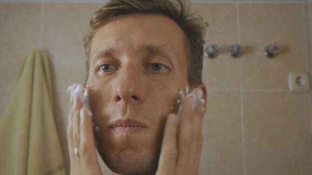 Close-up of caucasian man applying shaving foam on face in front of mirror. - 映像、動画