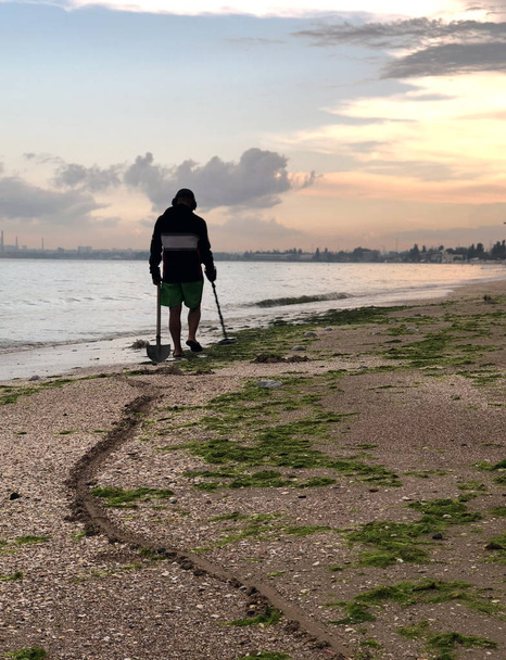 Pad van een shovel achter een man op zoek naar een edele metalen met behulp van een metaaldetector op het strand bij zonsondergang - Foto, afbeelding