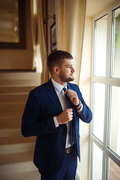 groom at wedding tuxedo smiling and waiting for bride in the hall of the hotel . Rich groom at wedding day. Elegant groom in costume and bow-tie. Groom in a suit holding buttonhole. - Fotó, kép