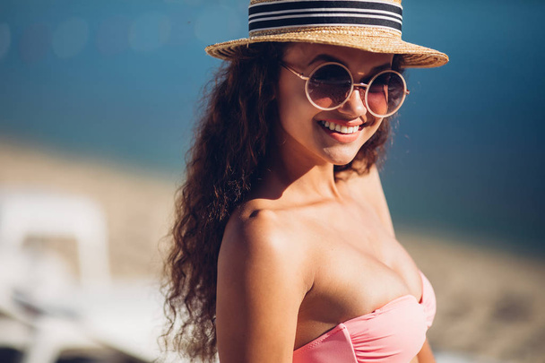 Coole hipster meisje in zomer stro hoed poseren naast exotische zomer strand hete zomer modeaccessoire, stijlvolle zonnebril, bikini. Sexy perfecte fit lichaam vrouw. Kopiëren, lege ruimte voor tekst. - Foto, afbeelding
