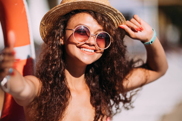 Portrait of fashionable long curly dark hair lady in pink bikini and straw hat making selfie posing beside exotic summer beach hot summer. - Fotografie, Obrázek
