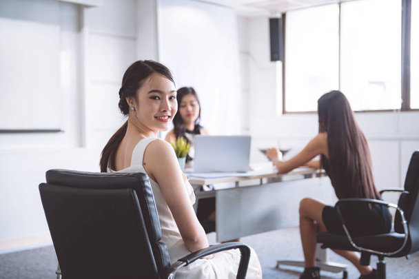 Young businesswomen brainstorming in office. Beautiful asian woman in office dress talking together over work with young woman looking at camera. Office woman at work concept. - Фото, изображение