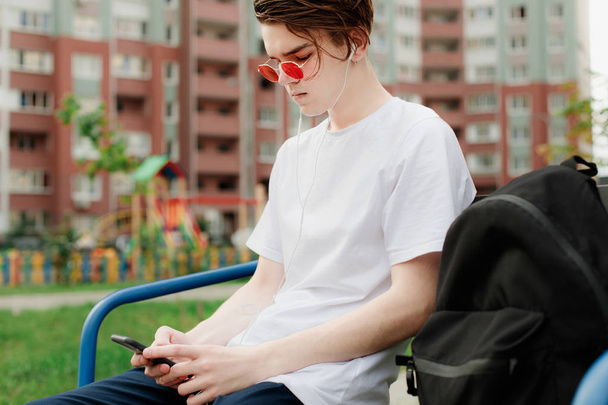 junger Mann mit roter Brille sitzt im Park und benutzt sein Handy. urbaner Stil - Foto, Bild