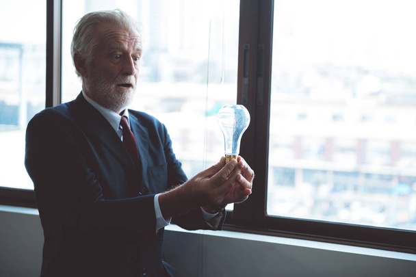 Senior business man holding light bulb. White male in suit looking happy. Half body shot. Business idea concept. - Fotografie, Obrázek