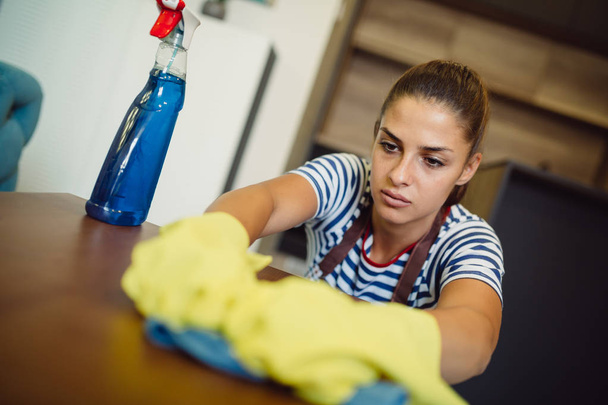 Piękna młoda kobieta podczas czyszczenia domu na sobie fartuch i rękawice - Zdjęcie, obraz