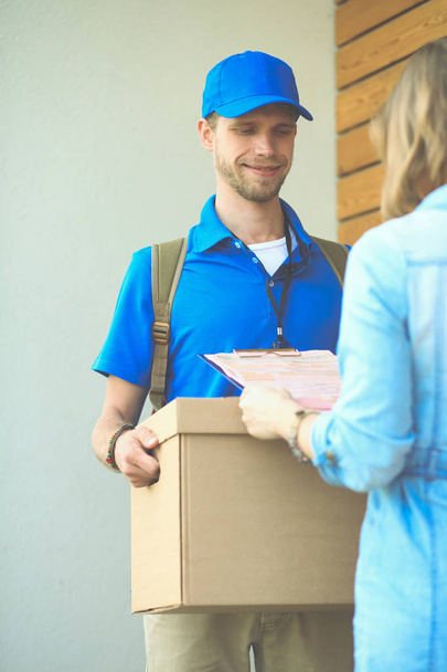 Smiling delivery man in blue uniform delivering parcel box to recipient - courier service concept. Smiling delivery man in blue uniform - Photo, image
