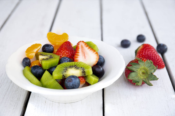 Verse fruitsalade in een wit bord op witte houten tafel. - Foto, afbeelding