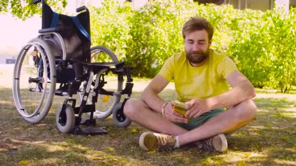 Happy young disable man sitting on the grass in the park - Footage, Video