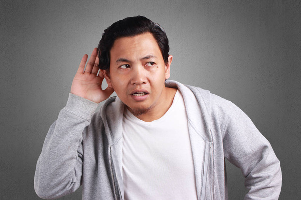Mladé asijské muži nosí sako naslouchání šepotu s legrační obličej. Zvědavý. Soustředěně Poslouchejte na šťavnaté drby. Konverzaci zprávy, narušení soukromí, izolované Grey - Fotografie, Obrázek