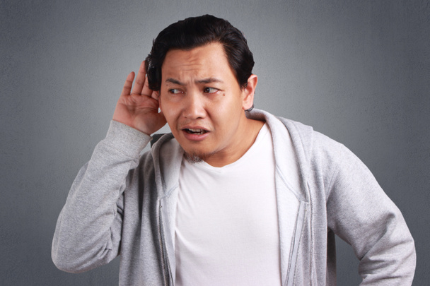 Giovani uomini asiatici che indossano giacca ascoltare sussurri con la faccia divertente. Curioso. Ascolta attentamente i pettegolezzi succosi. Notizie di conversazione, violazione della privacy, isolato su grigio
 - Foto, immagini