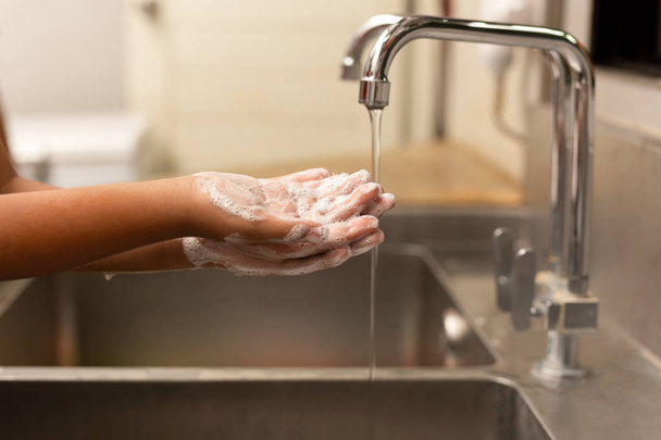 Child washing hands with liquid soap under the tap water in the kitchen sink. - Photo, Image