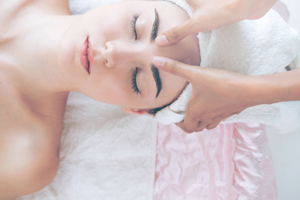 Mujer relajada tumbada en la cama de spa para el tratamiento de spa de masaje facial y de cabeza por terapeuta de masaje en un complejo de spa de lujo. Bienestar, alivio del estrés y concepto de rejuvenecimiento. - Foto, imagen