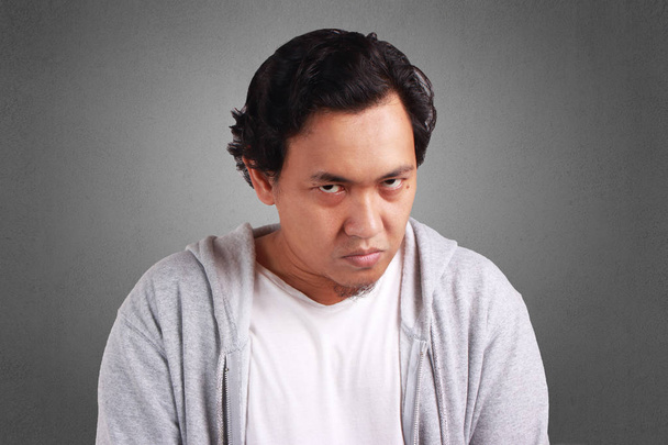 junger asiatischer Mann in weißem Hemd und grauer Jacke mit wütendem, verrücktem Gesichtsausdruck. Hintergrund auf grau. Kopf und Schulter aus der Nähe - Foto, Bild
