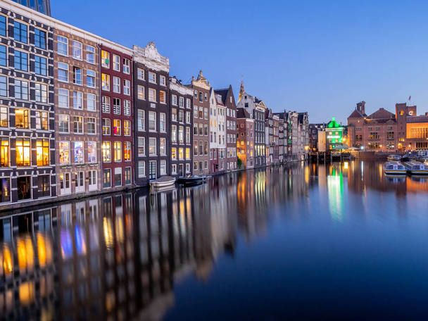 Casas de canal tradicionais no Damrak ao anoitecer em Amsterdã. Edifícios no canal são uma forma de arquitetura holandesa tradicional que agora é muito popular
. - Foto, Imagem