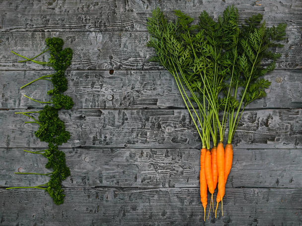 Куча моркови и петрушки на черном деревенском столе. Концепция вегетарианской пищи с натуральным сырьем. Вид с вершины. Плоский лежал
. - Фото, изображение