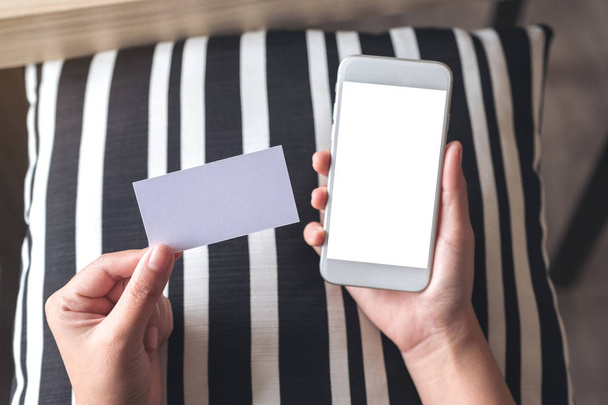 Imagem de maquete de vista superior de mãos segurando telefone celular branco com tela de desktop em branco e um cartão de visita vazio branco - Foto, Imagem