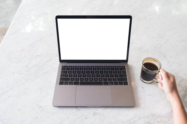 Вид зверху макет зображення руки, що тримає чашку кави і ноутбук з порожнім білим екраном робочого столу на мармуровому столі в кафе
 - Фото, зображення