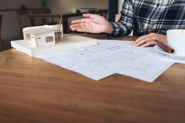Un architetto che lavora su un modello di architettura con carta da disegno e tazzina da caffè sul tavolo - Foto, immagini