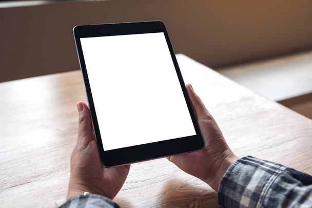 Wizerunek dłoni trzymających czarną tabletkę pc z białym ekranem na drewnianym stole - Zdjęcie, obraz